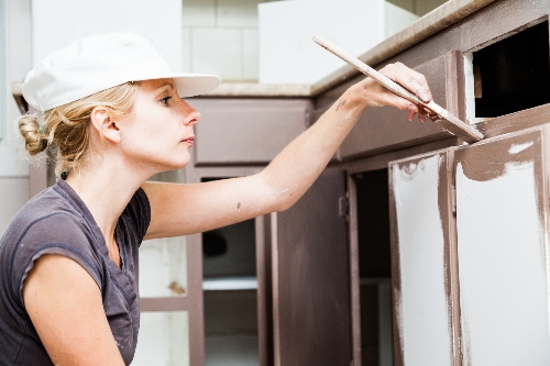 A woman paints her kitchen cabinets at home. 