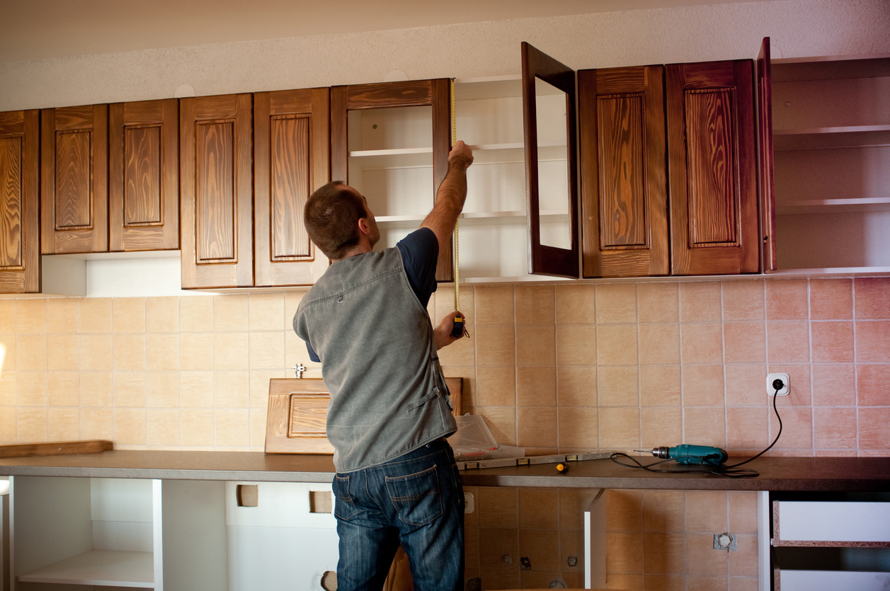 A man performing a complete cabinet refacing inside a residential kitchen.