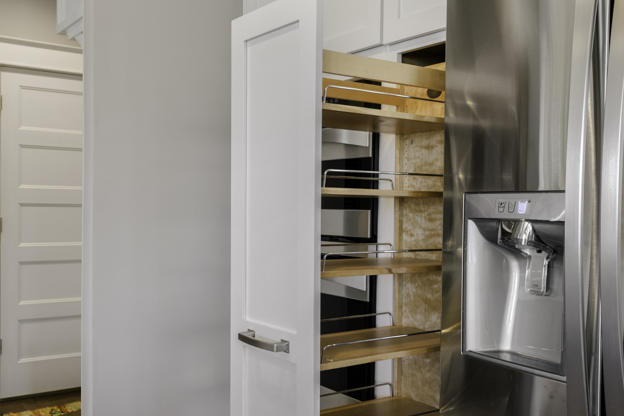 Kitchen with a stainless steel refrigerator beside a tall pull-out pantry cabinet featuring wooden shelves and metal rails. 