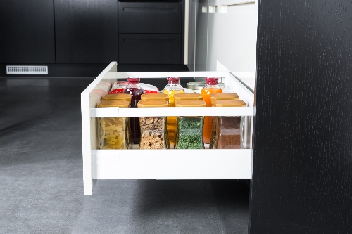 A kitchen drawer slides open to show dry foods separated into different clear jars.